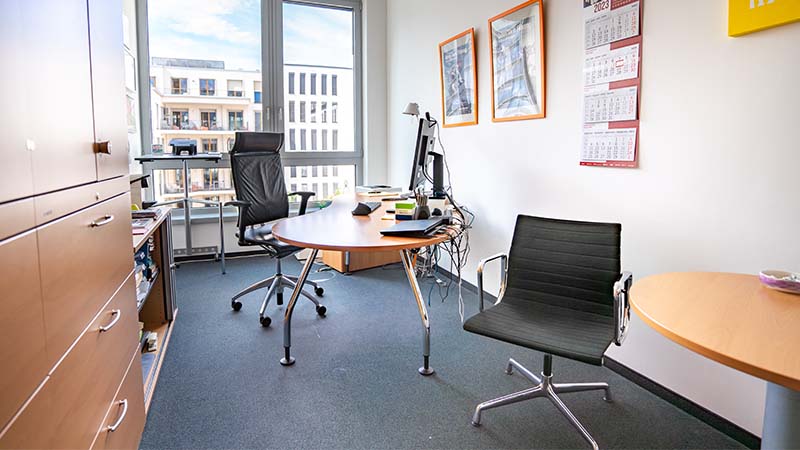 Modernes Büro mit Schreibtisch, schwarzem Drehstuhl, großem Fenster mit Blick auf Stadtgebäude und Wandkalendern